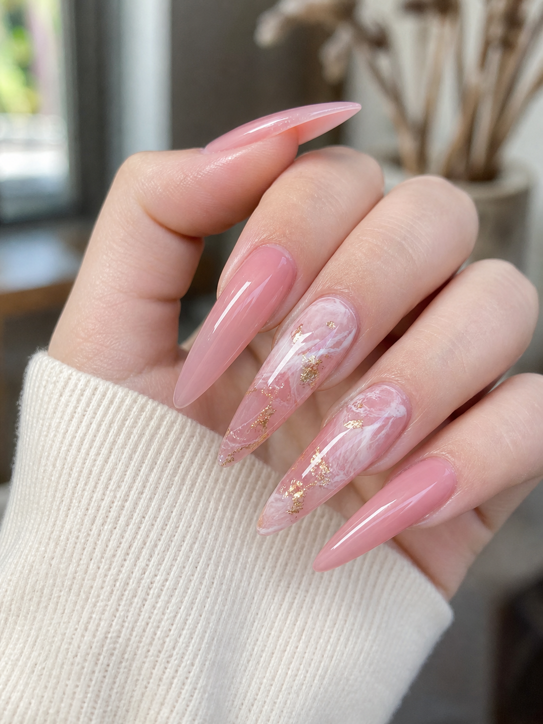 Ongles longs de forme stiletto avec un design marbré rose translucide, des tourbillons blanc laiteux et des accents de feuille d'or avec une finition brillante.