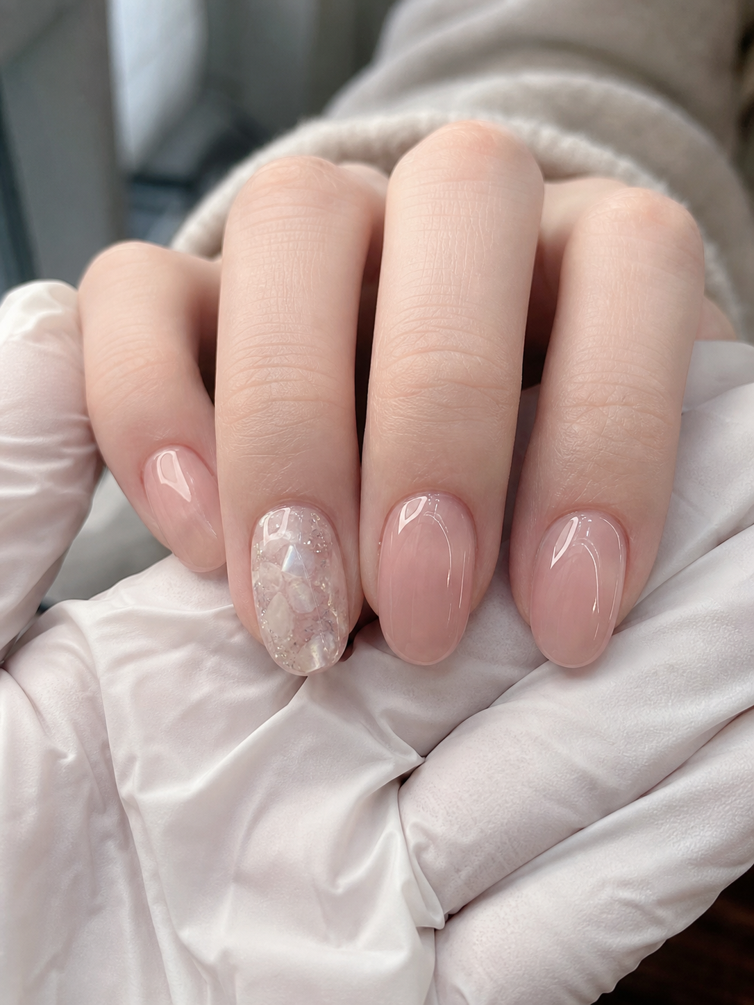 Unhas médias no formato redondo com base nude translúcida, detalhes em mármore branco, flocos de madrepérola e glitter prateado sutil.