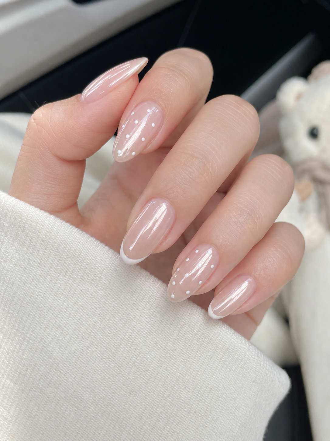 Unhas amendoadas médias com base nude translúcida perolada, exibindo francesinhas brancas finas e pequenas flores decorativas.